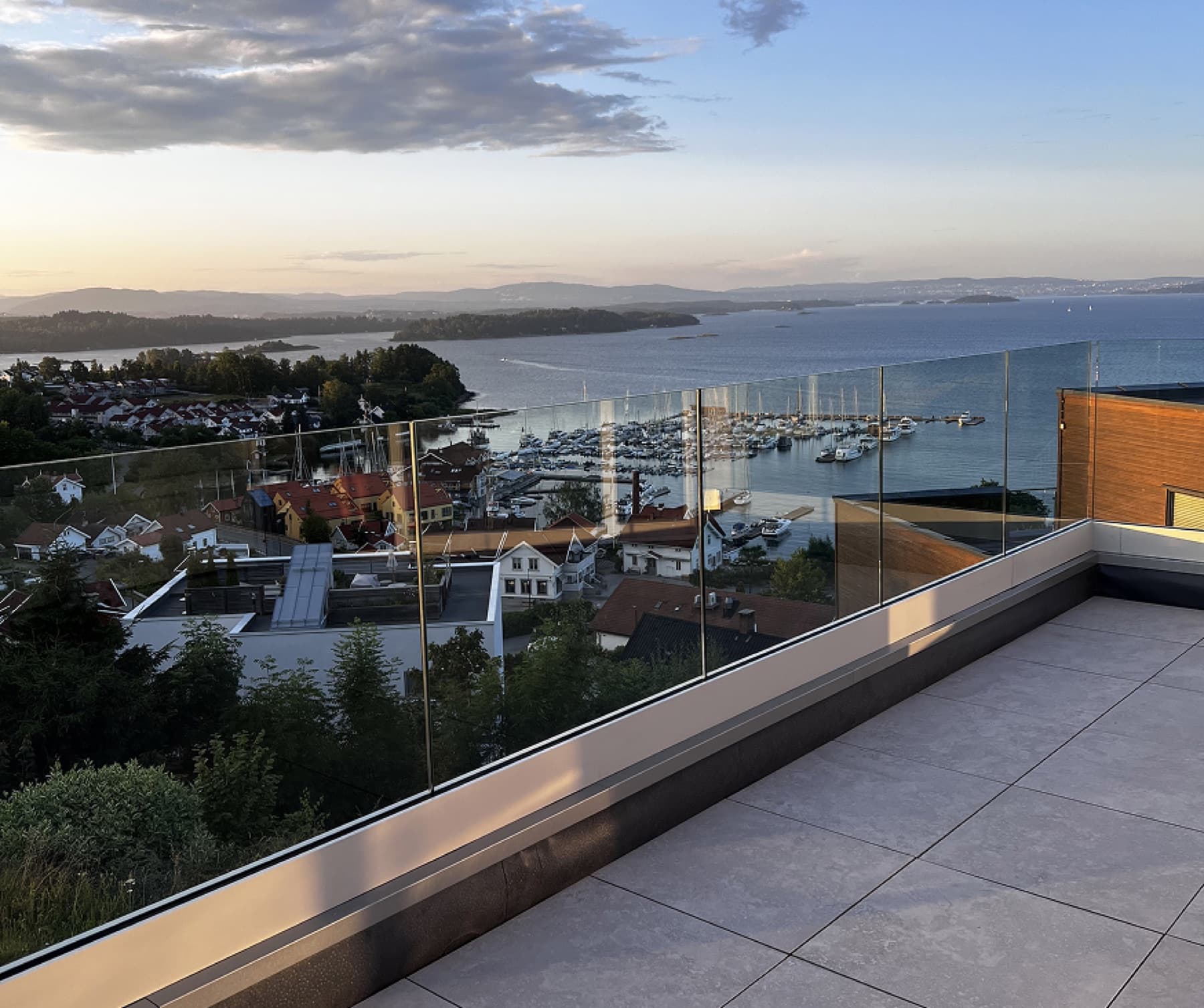 Ferdigmontert glassrekkverk på terrasse med utsikt over havn i solnedgang